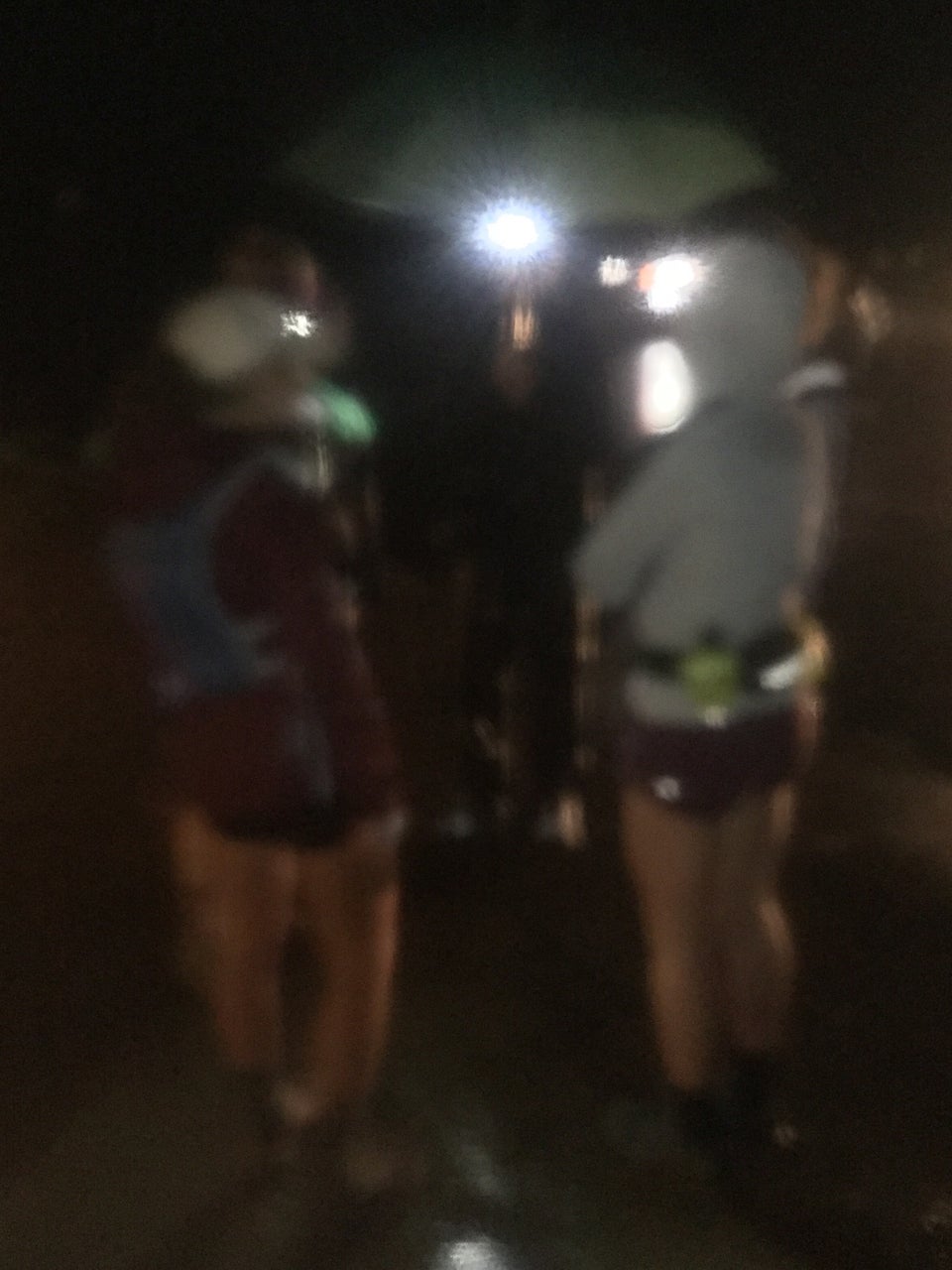 Blurry image of a few runners in rain gear and shorts on both sides of Bryan wearing a lit headlamp holding a green umbrella.